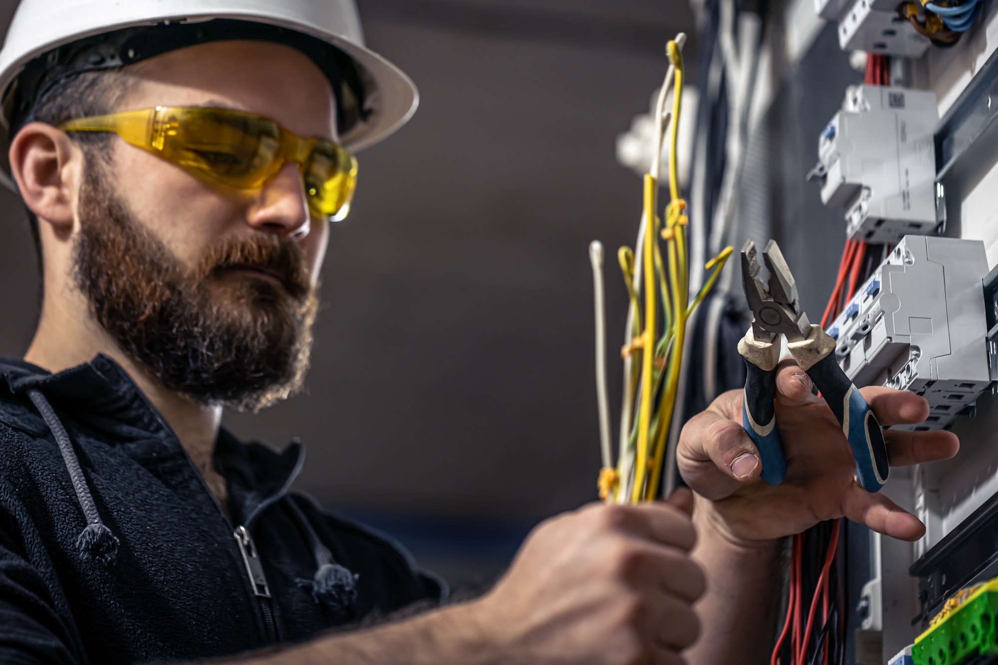 A male electrician works in a switchboard with an electrical connecting cable.